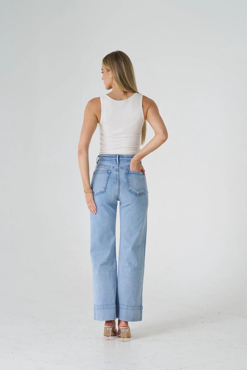 Woman wearing light blue jeans and a white top on a plain background