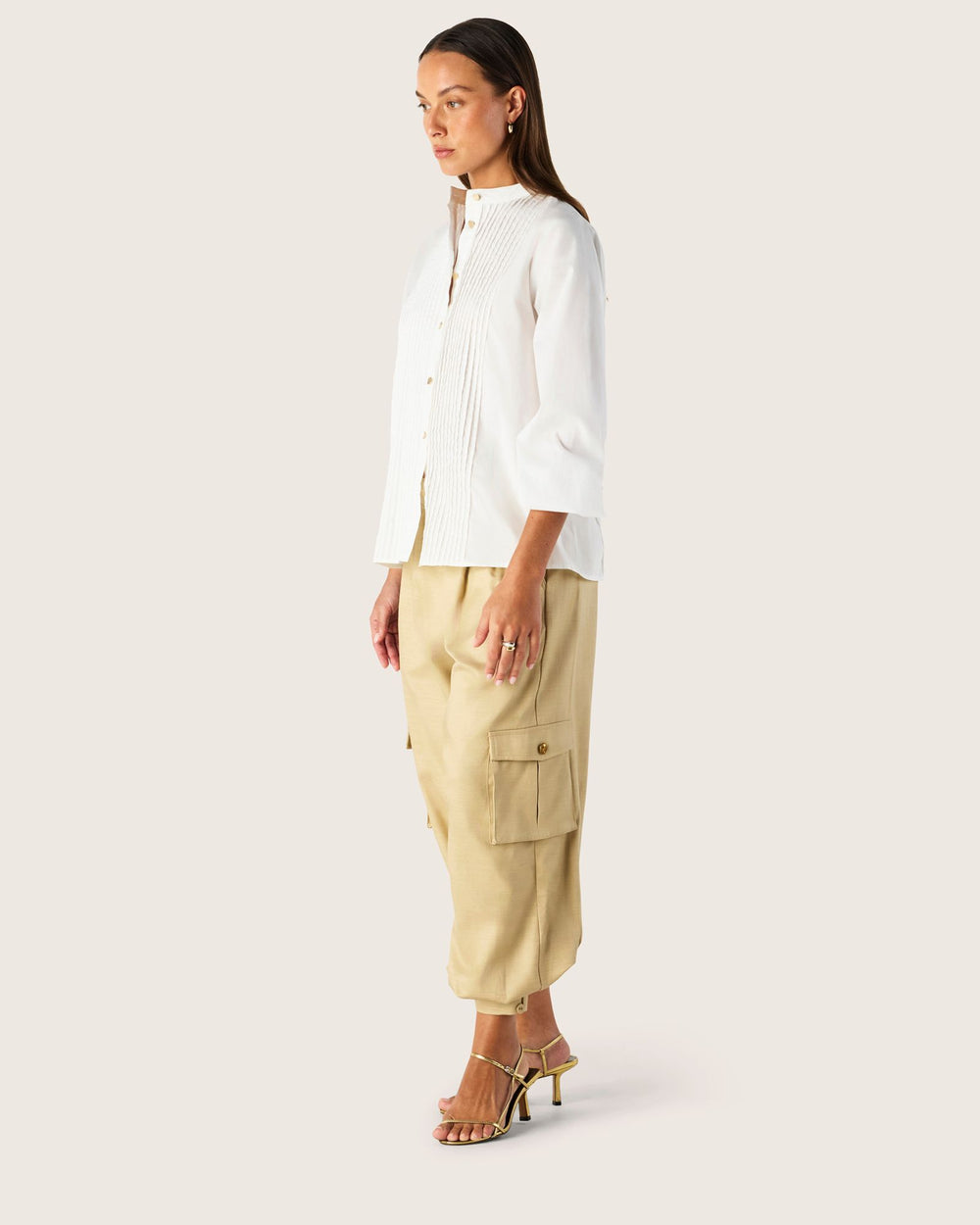 Woman wearing a white shirt and beige cargo pants on a plain background