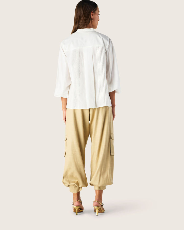 Woman wearing a white top and beige pants on a plain background
